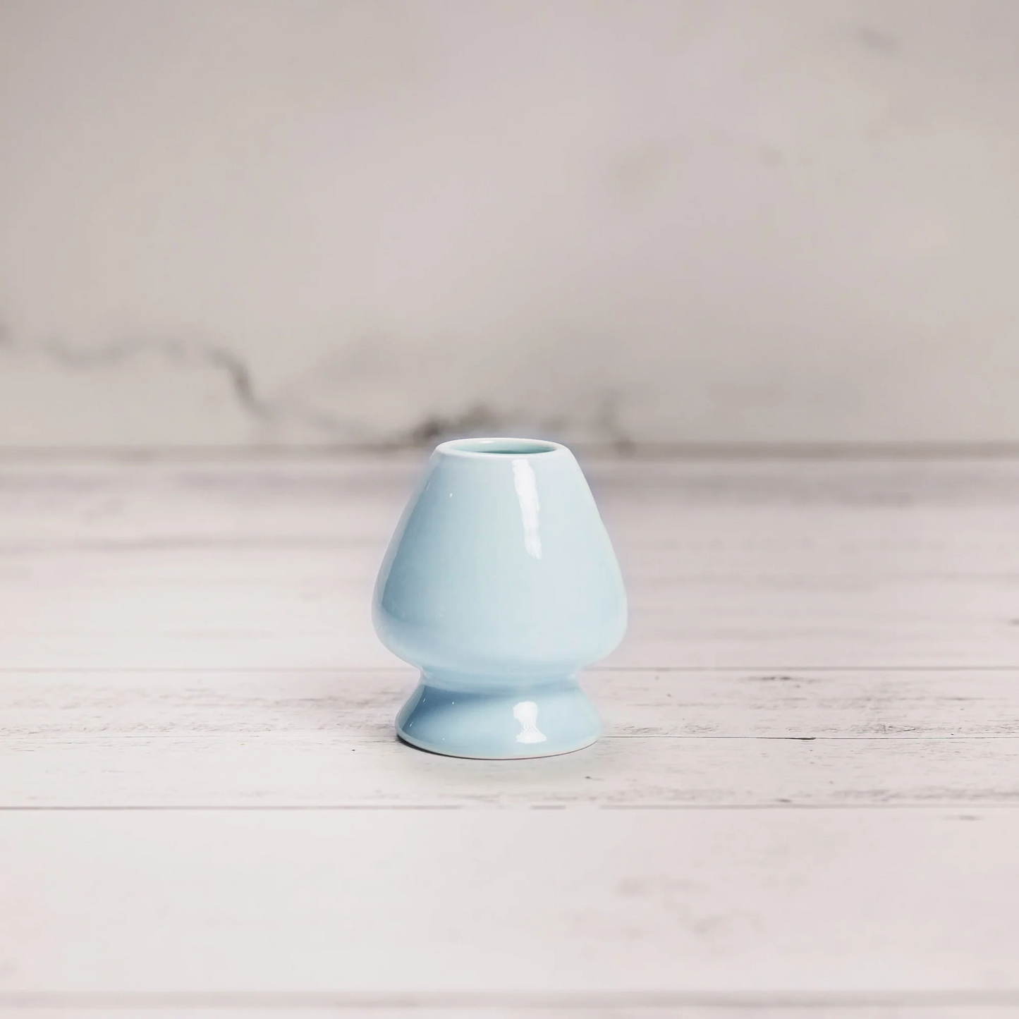 Light blue ceramic vase on a wooden surface with a light gray background