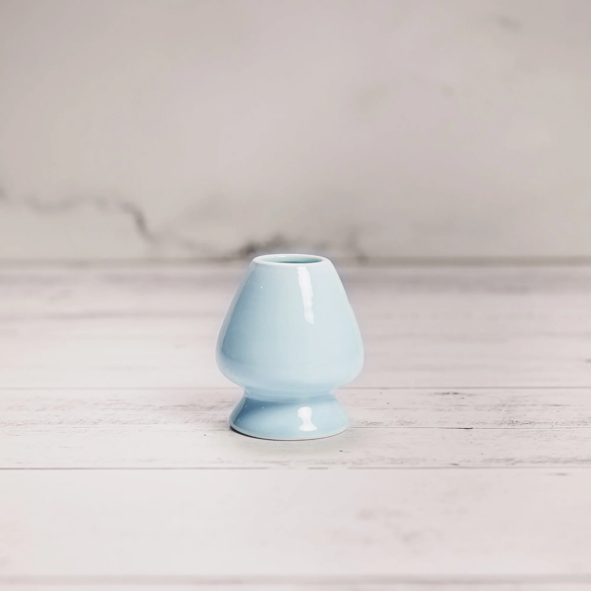 Light blue ceramic vase on a wooden surface with a light gray background