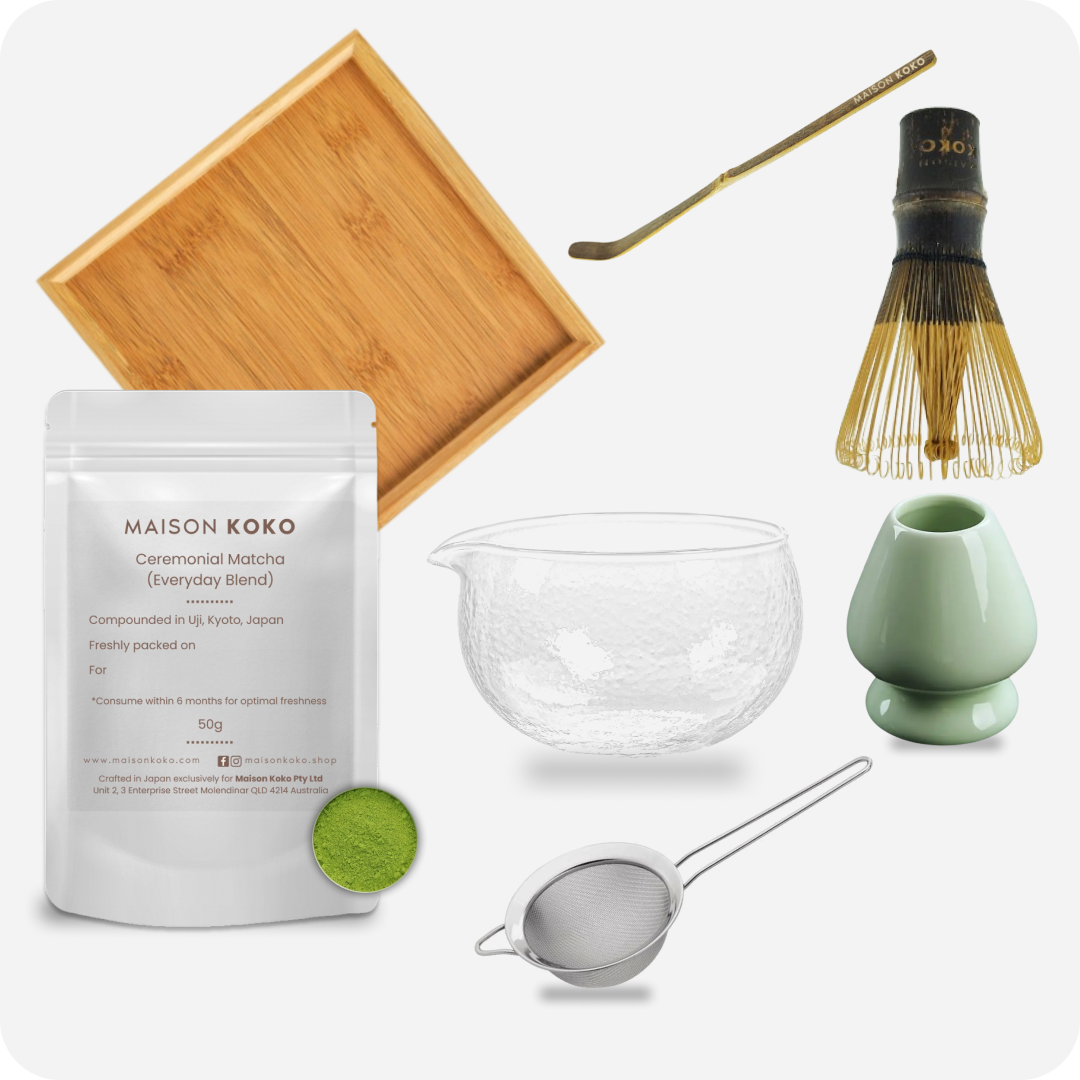 Matcha-making set with Maison Koko matcha powder, wooden tray, glass bowl, whisk, and other tools on a white background